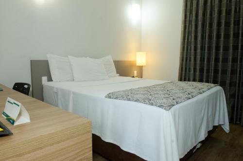 a bedroom with a large white bed and a table at Ímpar Suítes Expominas in Belo Horizonte