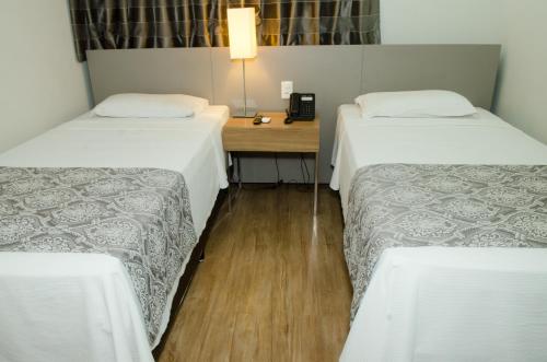a room with two beds and a desk with a phone at Ímpar Suítes Expominas in Belo Horizonte