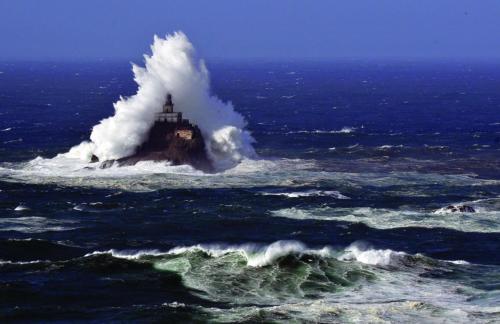 a lighthouse in the middle of the ocean with a wave at Webb's Scenic Surf in Cannon Beach