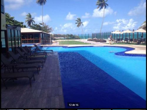 a large blue swimming pool with chairs and palm trees at Residência Tabatinga in Conde