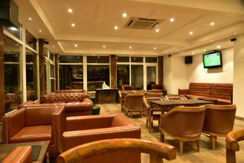 a restaurant with leather chairs and tables and a television at Asia Health Resorts & Spa in Dharamshala