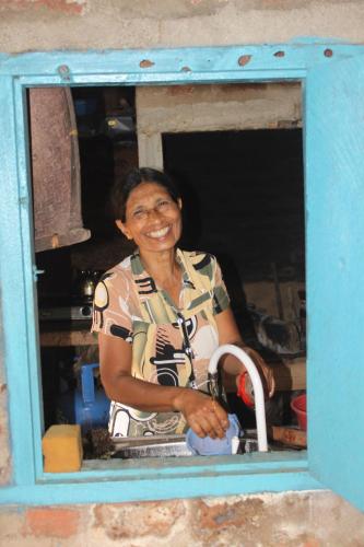 a woman is smiling while standing behind a window at Kataragama Homestay in Kataragama