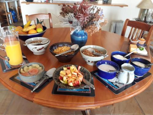 a wooden table topped with bowls of fruit and breakfast foods at Moonglow Guesthouse in Simonʼs Town