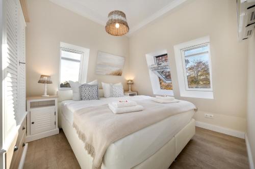 a white bedroom with a large white bed and two windows at Villa Strandblick 12 in Zingst
