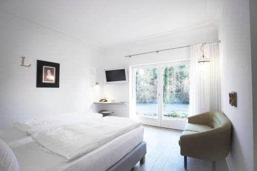 a white bedroom with a bed and a chair and a window at Landhaus am See in Garbsen
