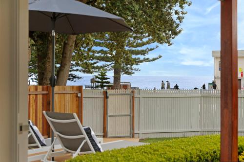 a patio with chairs and an umbrella and a fence at The Beach House North Wollongong in Wollongong