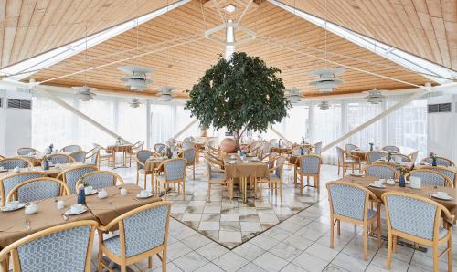 un salón de banquetes con mesas, sillas y un árbol en Living Hotel Nürnberg, en Núremberg