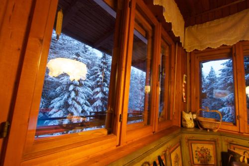 a window in a cabin looking out at a snow covered tree at Villa La Brisa in Predazzo