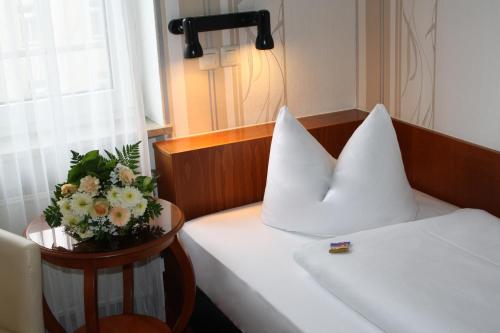 a bed with white pillows and a table with flowers on it at Hotel Berlin in Leipzig
