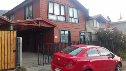 une voiture rouge garée devant une maison rouge dans l'établissement Hospedaje María Elena, à Coyhaique