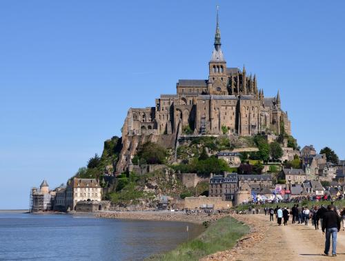 Leute, die am Strand vor einem Schloss spazieren in der Unterkunft Huttopia Baie du Mont Saint Michel in Baguer-Pican