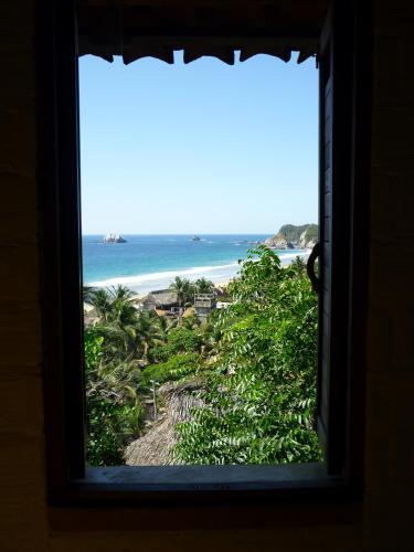 a window with a view of a beach and the ocean at LA LOMA LINDA, Bungalows, Yoga and Feldenkrais, STARLINK INTERNET in Zipolite
