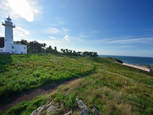 a lighthouse on a hill next to the ocean with a train at Smile Hotel Hachinohe in Hachinohe