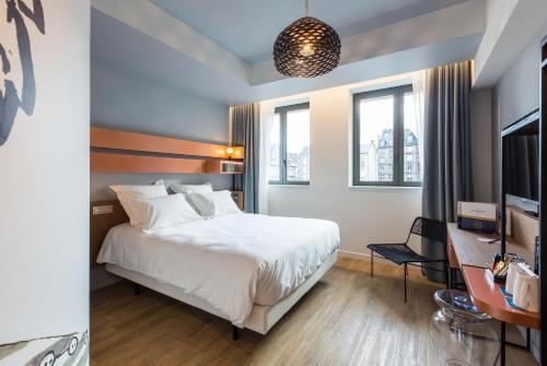 a bedroom with a bed and a desk and windows at Golden Tulip Saint Malo– Le Grand Bé in Saint Malo