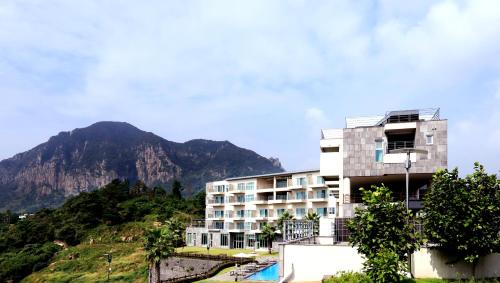 a building on a hill with a mountain in the background at Y Resort Jeju in Seogwipo