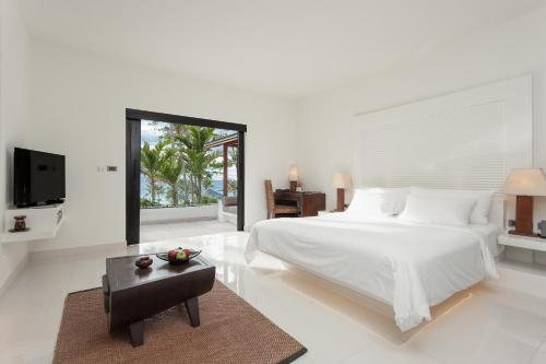 a white bedroom with a large bed and a table at The Racha in Ko Racha Yai 