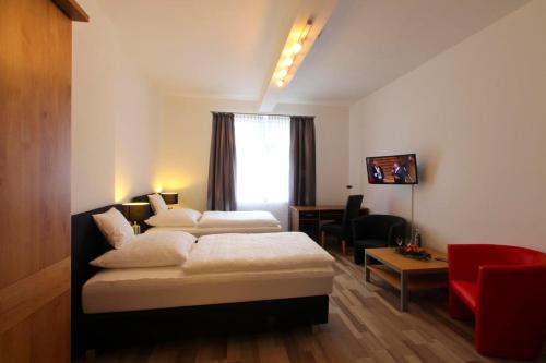 a hotel room with two beds and a red chair at Hotel Jammerkrug in Gladbeck