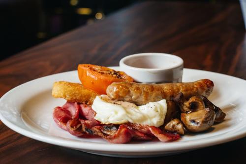 a plate of breakfast food with bacon sausage and a tomato at The Mount Country Manor Hotel & Golf Wolverhampton in Wolverhampton