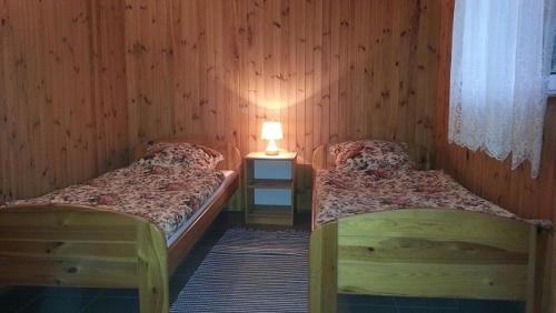 two beds in a wooden room with a lamp at Domki Letniskowe Kobyłocha in Kobyłocha