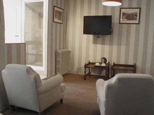 a living room with two chairs and a television at Hôtel La Licorne & Spa in Lyons-la-Forêt