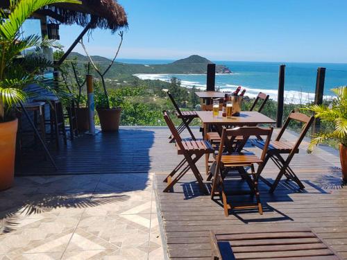 a wooden deck with tables and chairs and the ocean at Pousada Hostel Albergue Explorer in Praia do Rosa