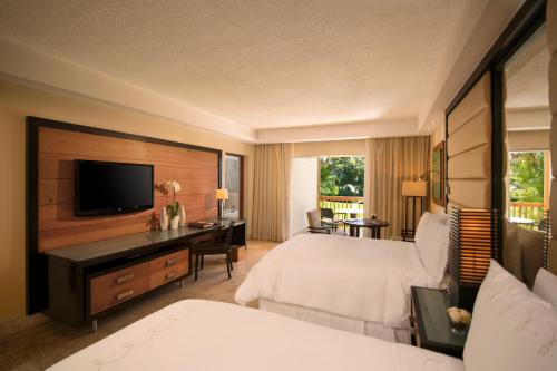 a hotel room with two beds and a desk with a television at Casa de Campo Resort & Villas in La Romana
