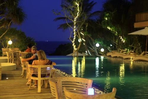 a couple sitting at a table by a pool at night at Thaproban Pavilion Waves in Unawatuna