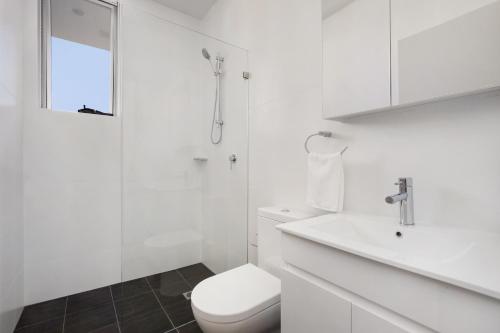 a white bathroom with a toilet and a sink at Bondi Beach Studio Penthouse Suite + Balcony in Sydney