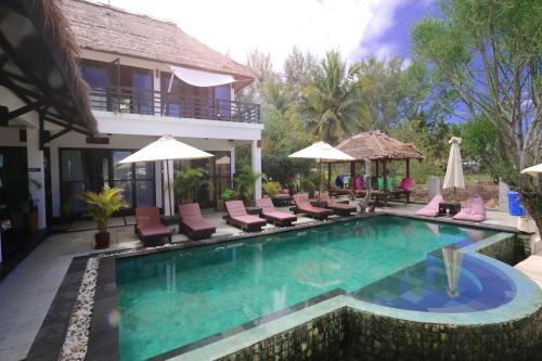 a pool at a resort with chairs and umbrellas at Villa Julius in Gili Trawangan