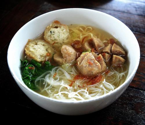 a bowl of soup with meat and noodles on a table at BeOne House Jogja in Yogyakarta