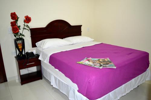 a bed with a purple blanket and a table with flowers at Sol Caribe Hotel in Soledad