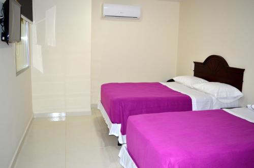 two beds in a room with purple sheets at Sol Caribe Hotel in Soledad