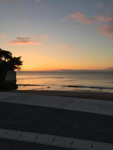 a sunset over the ocean with a tree on the beach at Traveler's Wharf Shichigahama in Shichigahama