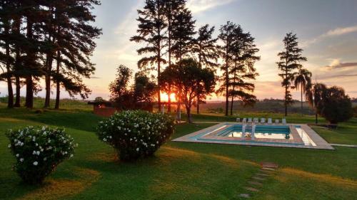 uma piscina num quintal com árvores e o pôr do sol em Hotel Pousada La Vierro em Ponta Grossa