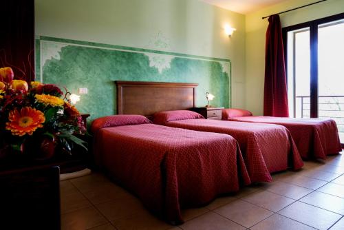 una camera con tre letti con lenzuola rosse e fiori di Hotel Salento a Specchia