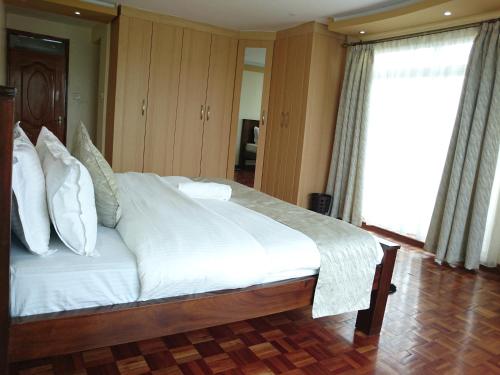 a bedroom with a large bed with white sheets and pillows at Yaya Brooks - Tomax in Nairobi