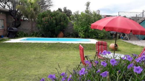 um quintal com um guarda-sol vermelho e cadeiras e uma piscina em La Chacarita apart em San Fernando del Valle de Catamarca