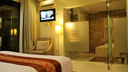 a hotel room with a bed and a tv and a chair at The Nibbana Villas in Seminyak