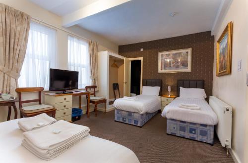 ブラックプールにあるMaples Hotelのベッド2台、デスク、テレビが備わるホテルルームです。