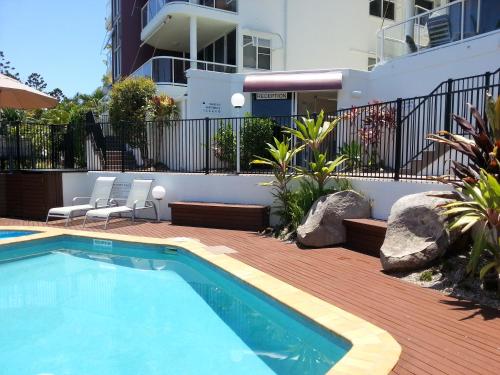 a swimming pool with two chairs next to a building at Bali Hai Apartments Noosa in Noosa Heads