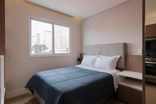 um quarto com uma cama com um cobertor azul e uma janela em Studio próximo ao shopping Curitiba, Wifi, TV a Cabo e Cozinha completa. em Curitiba