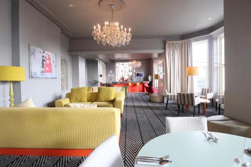 a restaurant with yellow chairs and tables and a chandelier at Citrus Hotel Eastbourne by Compass Hospitality in Eastbourne