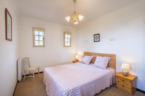 a white bedroom with a bed and a chair at La Maison des Roches in Gordes