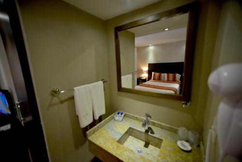 a bathroom with a sink and a mirror and a bed at Hotel Posada La Sorgente in Puerto Iguazú