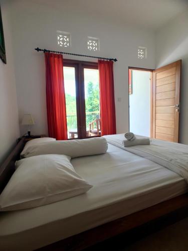 a bedroom with two beds with red curtains and a window at Uluwatu Made Guesthouse in Uluwatu