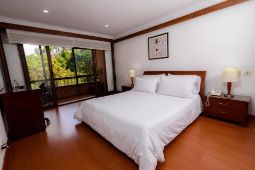 a bedroom with a white bed and a large window at Travelers Condominio Plenitud in Bogotá