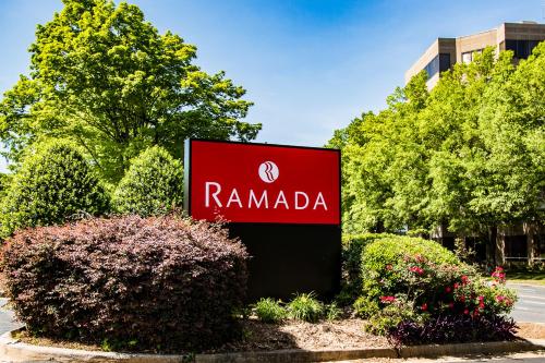 a sign for a rammada company in front of trees at Ramada by Wyndham Gainesville in Gainesville