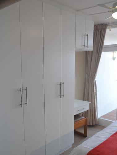 a bedroom with white cabinets and a desk at Driftsands Sea View Flats in Uvongo Beach
