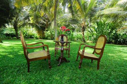 three chairs and a table with a vase with flowers at Old Parkland Hostel in Galle