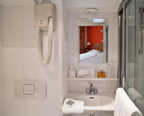 La salle de bains blanche est pourvue d'un lavabo et d'un miroir. dans l'établissement Tonic Hôtel du Louvre, à Paris